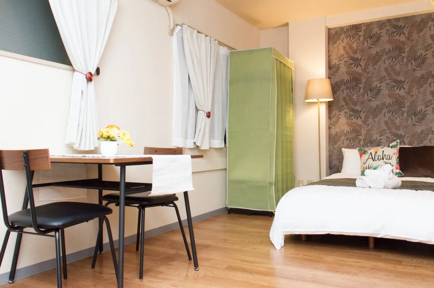 Ein Hotelzimmer mit einem Bett, einem Schreibtisch mit Stühlen, einem grünen Wandschrank und einer Wand mit floralem Muster.