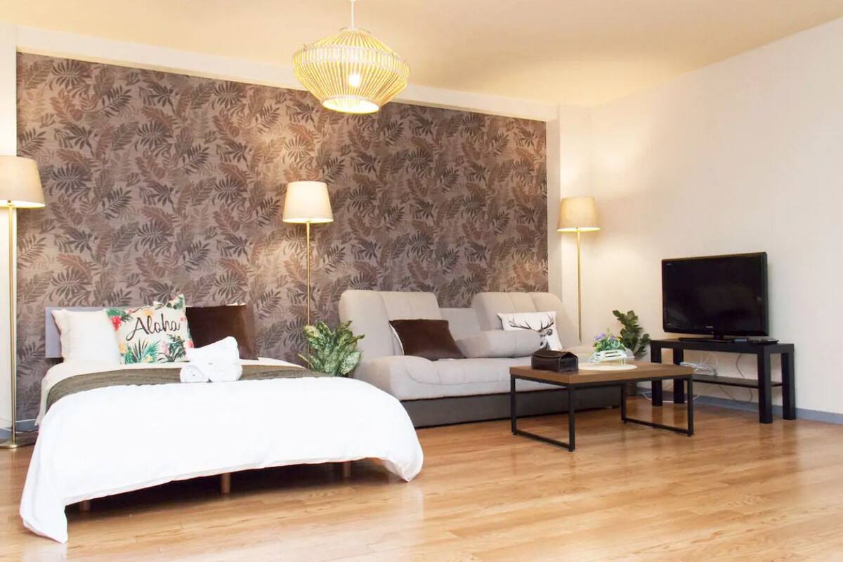 Un salon moderne comprenant un lit, deux canapés, une table basse, un téléviseur et un mur décoré d’un motif.