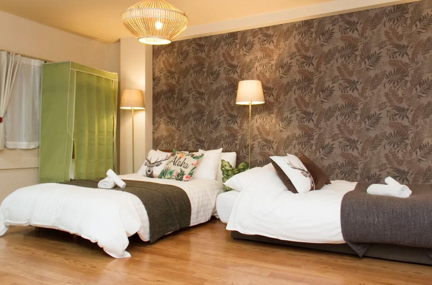 Una camera d'albergo con due letti, un armadio verde e una parete con motivi floreali.