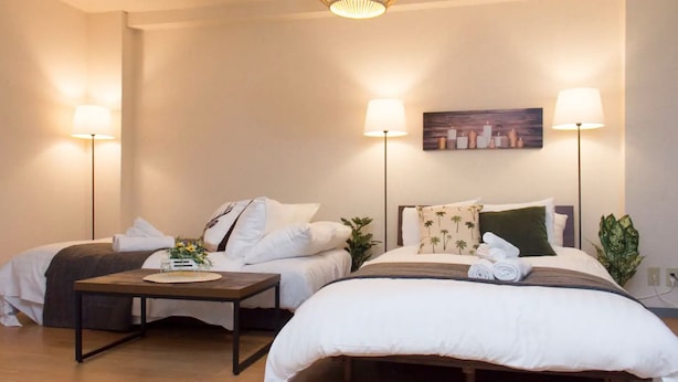 Quarto de hotel com duas camas, uma mesa de cabeceira com abajur, um quadro na parede e uma planta.