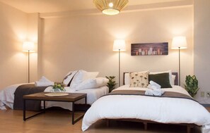 A hotel room with two beds, a nightstand with a lamp, a painting on the wall, and a plant. - Comfort Self Hotel First Breath (Osaka)