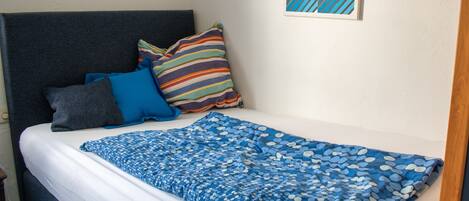 Una cama con una colcha azul estampada, un cojín a rayas y un cojín azul.