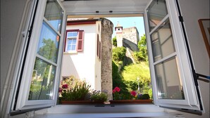An open window with a view of a stone tower and a garden with flowers. - Hotel Herberge zur Traube (Bad Wimpfen)
