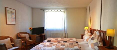 A hotel room with a bed, two chairs, a television, a lamp, and a window with curtains.