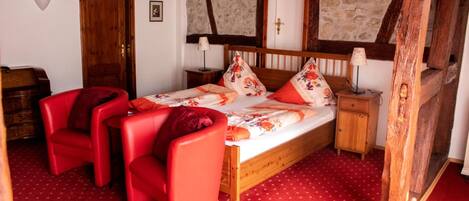 A bedroom with a wooden bed, red chairs, a wooden nightstand, and a red carpet.
