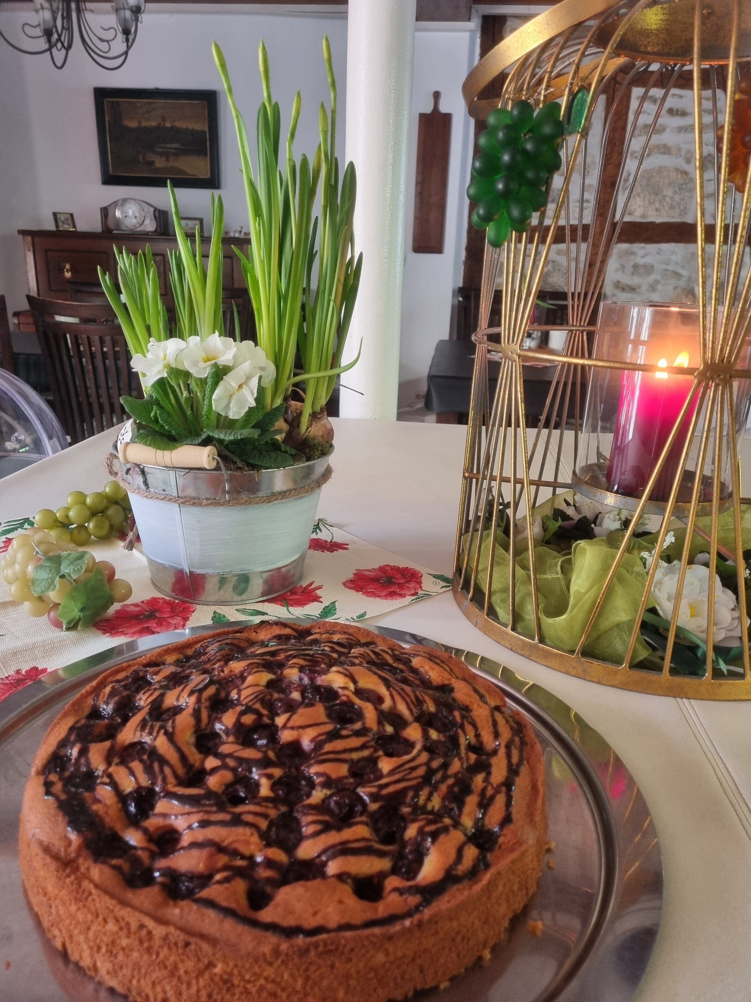 A table with a chocolate-topped cake, a floral centerpiece, and a candle in a decorative cage.