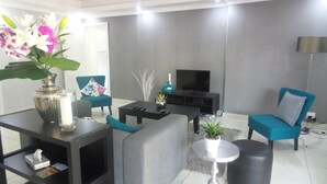 A modern living room with a sofa, armchairs, a coffee table, a TV, and a vase with flowers. - The Grand Orchid Guesthouse (Durban North)