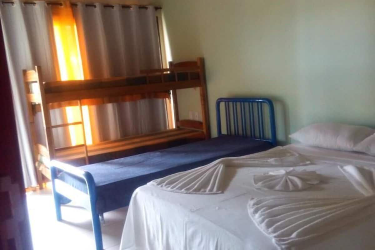 A room with bunk beds, a single bed, and a window with curtains.