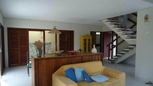 A living room with a yellow sofa, a wooden coffee table, and a staircase leading to an upper level. - Suites Solanas de Porto - Porto de Galinhas (Ipojuca)