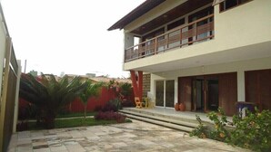 A modern two-story building with a balcony, a tiled courtyard, and a red wall. - Suites Solanas de Porto - Porto de Galinhas (Ipojuca)