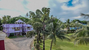 A two-story building with a purple facade, a curved roof, and a well-maintained lawn with palm trees.
