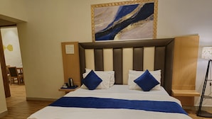 A hotel room with a large bed, two pillows, a bedside table with a lamp, and a painting above the bed.
