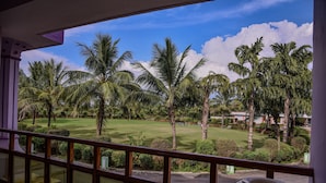 A view of a well-maintained golf course with palm trees and manicured lawns, viewed from a balcony with a wooden railing.