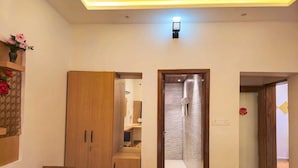 A room with a wooden wardrobe, a shower area, and a small seating area.