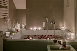 Eine Badewanne mit Rosenblüten, Kerzen und zwei Weingläsern.