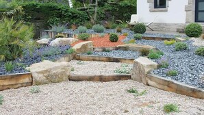 Ein angelegter Garten mit einem weißen Gebäude, Steinmauern und verschiedenen Pflanzen.