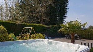 Ein Whirlpool in einem Garten mit Schaukel, Palmenbaum und einer Sitzgruppe im Freien.