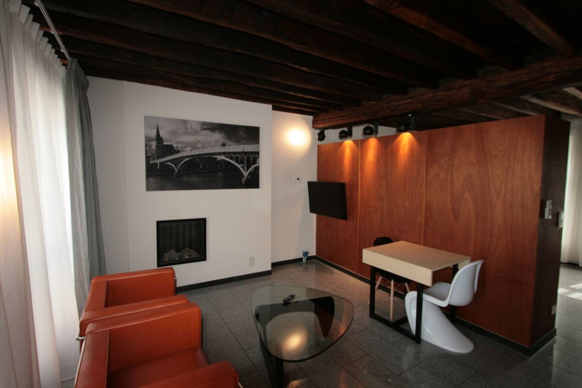 Een moderne woonkamer met een bank, een glazen salontafel, een eethoek met tafel en stoelen, een open haard en een aan de muur bevestigde televisie.