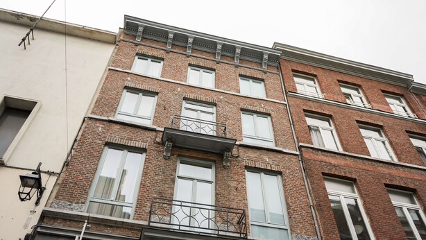 A multi-story building with a brick facade, multiple windows, and a balcony with metal railings.