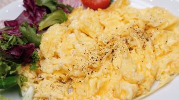 A plate of scrambled eggs with a side of mixed greens and a tomato, and another plate with bacon.