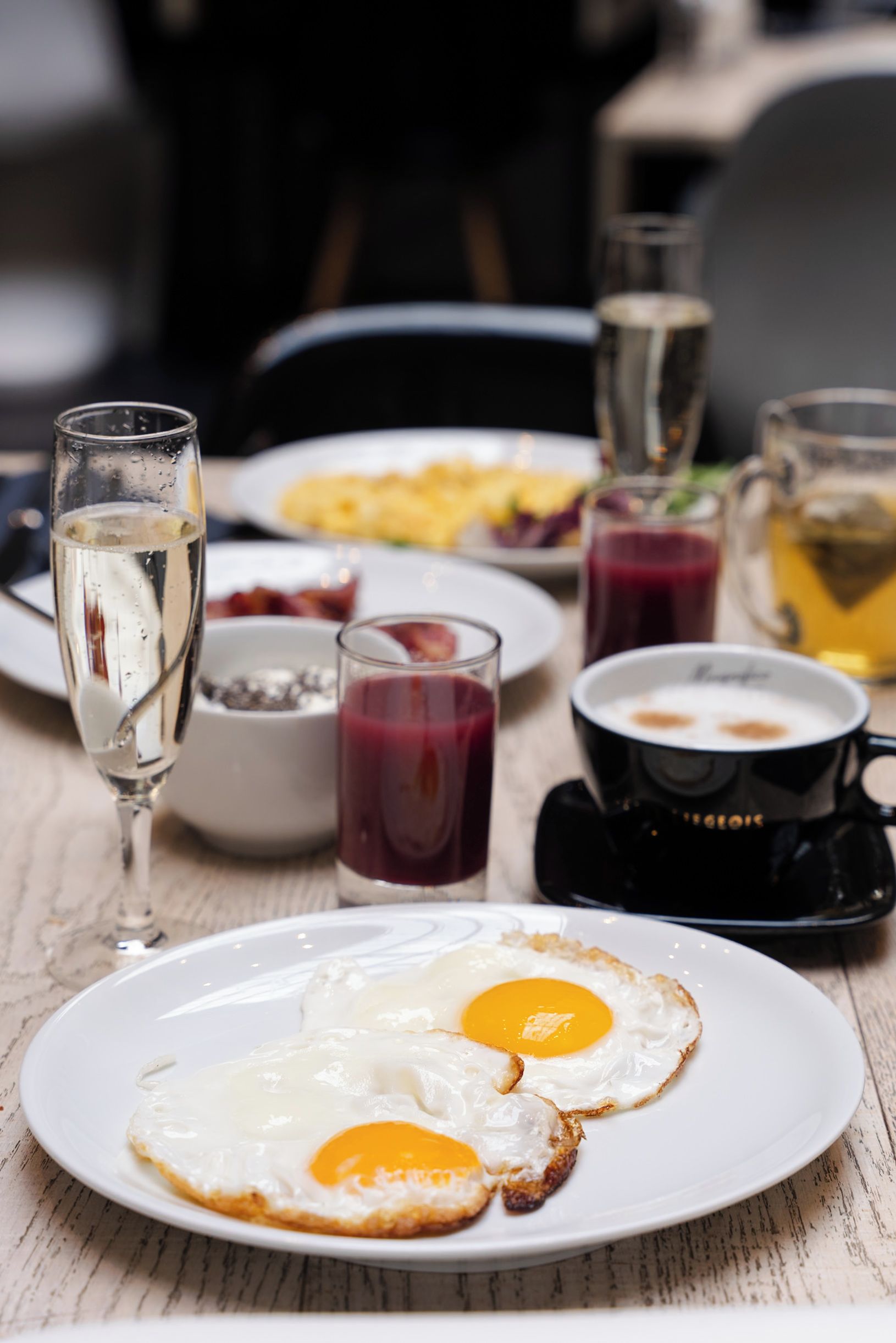 A breakfast setting with a plate of fried eggs, a glass of water, and a coffee cup on a wooden table.