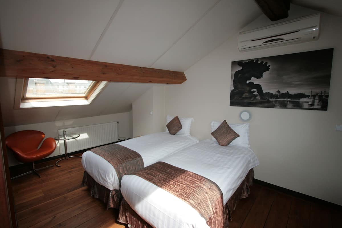 Een slaapkamer met twee bedden, een dakraam, een rode stoel en een schilderij aan de muur.