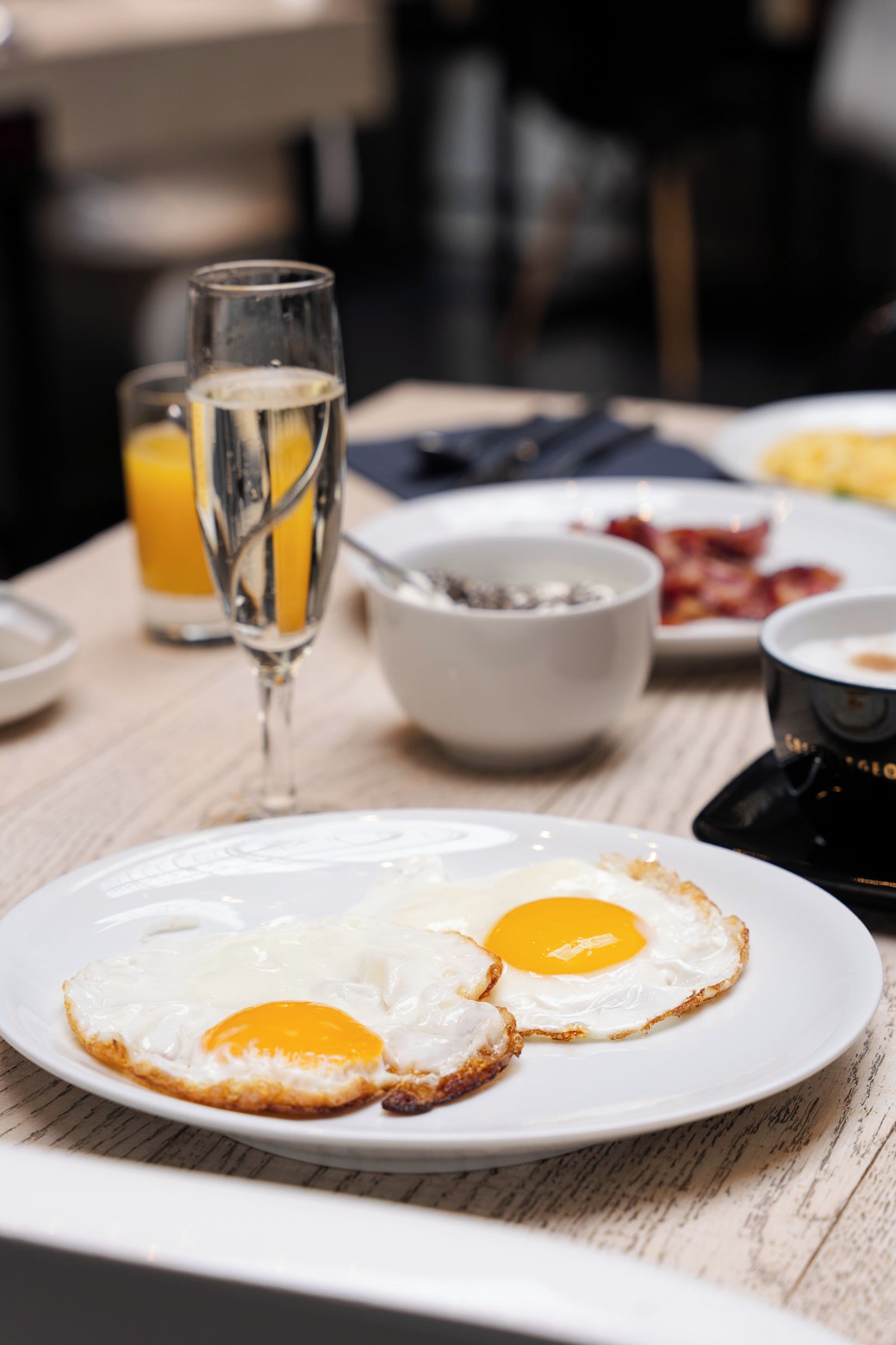 A breakfast setting with two fried eggs on a plate, a glass of orange juice, and a coffee maker on the table.