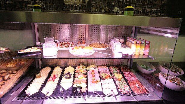Un buffet proposant une variété de plats et de boissons, présentés dans une vitrine, avec en arrière-plan une vue sur le paysage urbain.