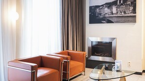 A living room with a sofa, a glass coffee table, a television, and a cityscape painting on the wall. - Amosa Liège City Centre Apart Regence 10 (Liege)