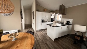 Una cocina moderna con armarios blancos, una isla central y una zona de comedor con mesa de madera.