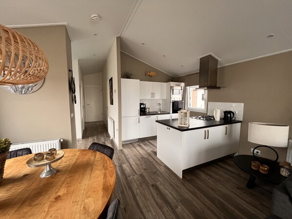 Una cocina moderna con armarios blancos, una isla central y una zona de comedor con mesa de madera.