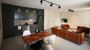A modern kitchen with dark cabinets, a dining table, and a sofa in a living area.