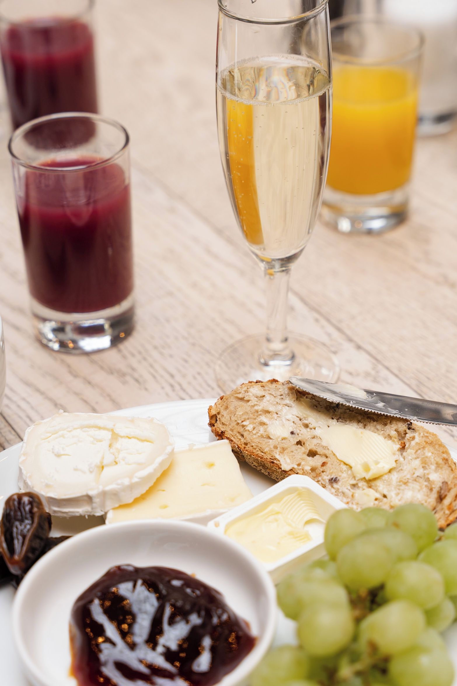Un tavolo con un piatto di formaggio, cracker e uva, insieme a bicchieri di succo e una bottiglia di champagne.