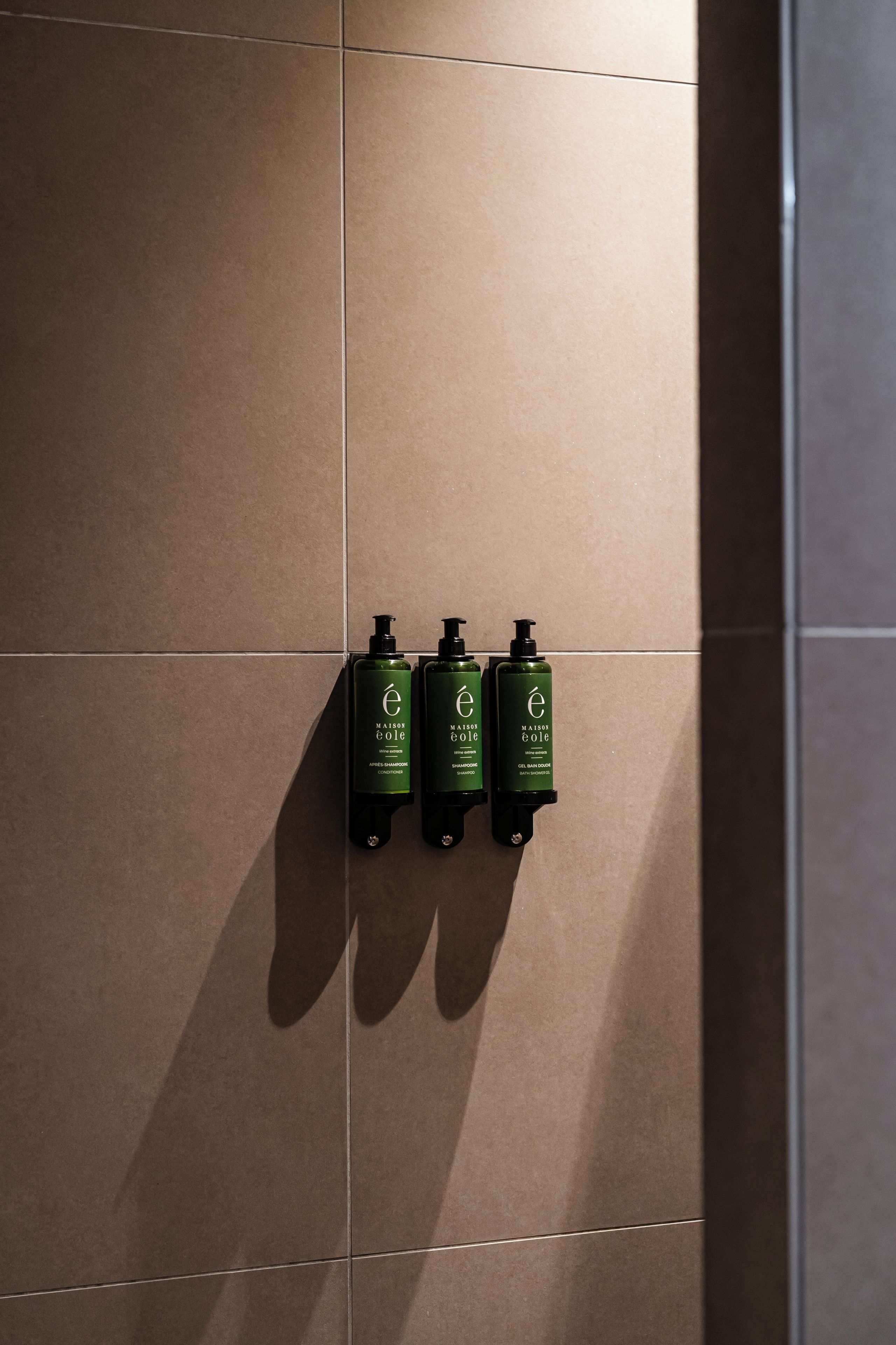 Un dispenser a parete con tre flaconi di shampoo e balsamo Maison eole.