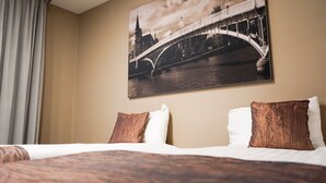 A hotel room with a bed, two pillows, a large framed picture of a bridge, and a curtain.