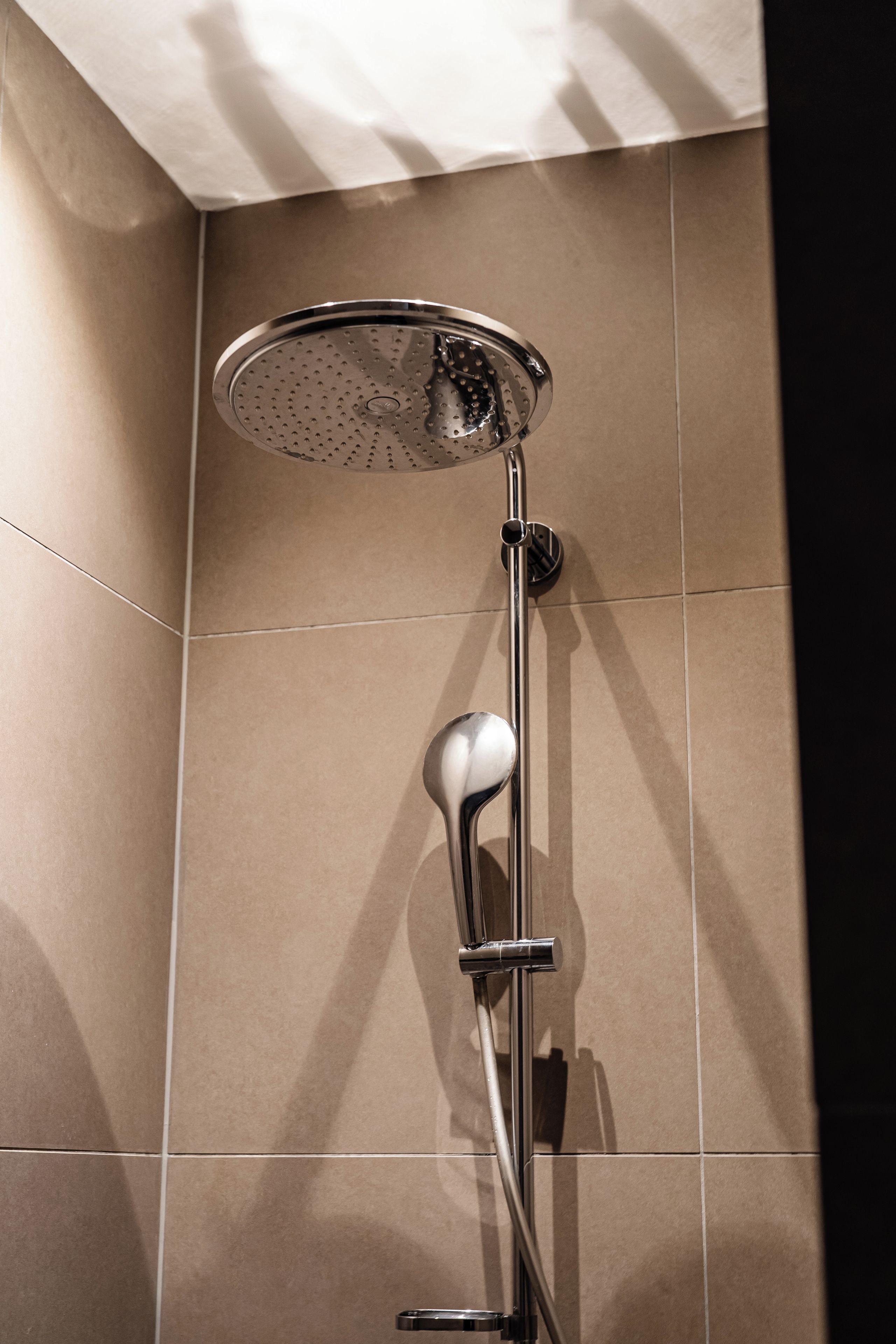 Een douche met een ronde douchekop en een handdouche.