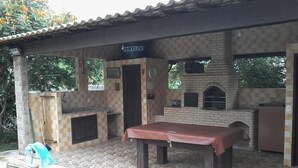 An outdoor patio with a pool table, a brick oven, and a covered seating area. - Recanto Suítes (Araruama)