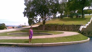 A woman in a purple dress standing by a circular water feature with a stone wall and a grassy area. - Recanto Suítes (Araruama)