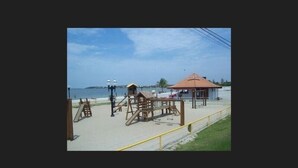 A beach with wooden play structures, a small pavilion, and a lifeguard tower. - Recanto Suítes (Araruama)