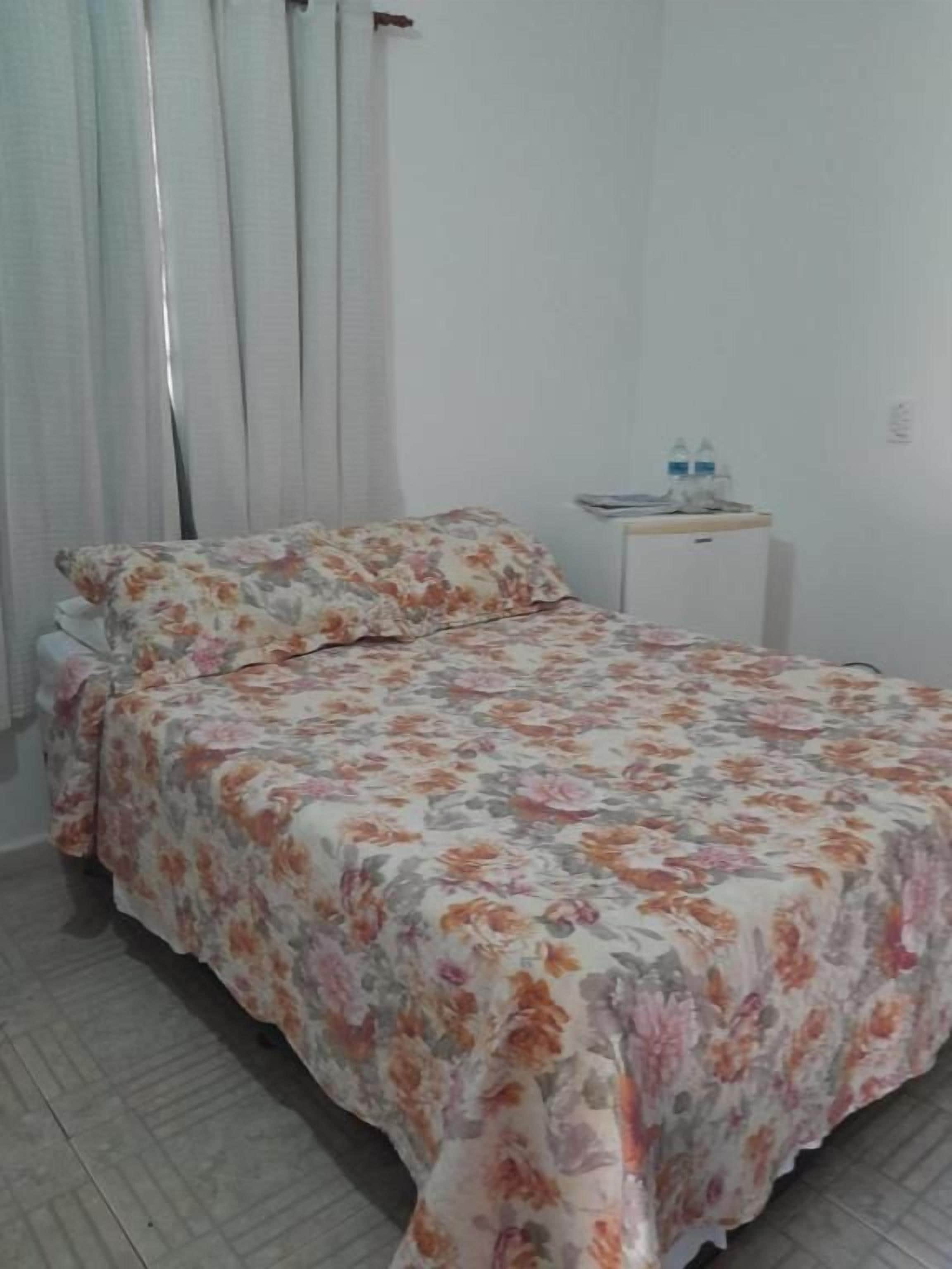 A bedroom with a bed, a nightstand, and a window with curtains.