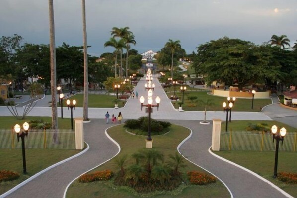 A pathway leading to a building with a central light fixture, surrounded by palm trees and well-maintained landscaping. - Recanto Suítes (Araruama)