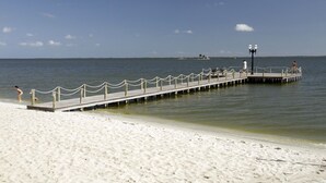 A beach with a wooden pier extending into the water, featuring a railing and a lamp post. - Recanto Suítes (Araruama)