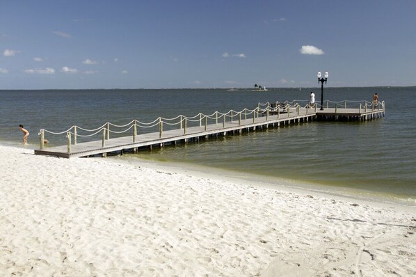 Ein Strand mit einer hölzernen Pier, die sich ins Wasser erstreckt, inklusive Geländer und einer Laterne.