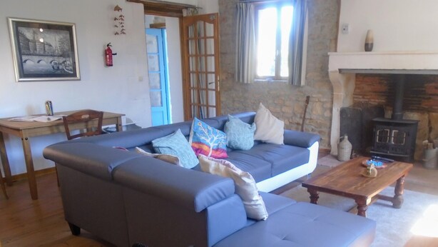 A living room with a blue sofa, a wooden coffee table, a fireplace, and a stone wall. - Rural Farmhouse with Spacious Garden near Charroux (Charroux)