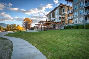 A modern multi-story building with a covered outdoor seating area, a well-maintained lawn, and a clear sky.