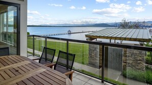 A balcony with a view of a lake and mountains, wooden furniture, and a stone wall. - Steps from Lake, 1st Floor - Seasons at Sandpoint (Sandpoint)