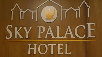 Une enseigne pour l’hôtel Sky Palace, avec un logo représentant un oiseau stylisé et une rangée de maisons au-dessus du nom de l’hôtel.