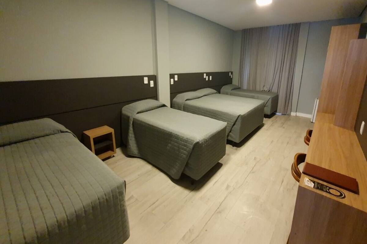 A hotel room with three single beds, a wooden desk, and a small nightstand.