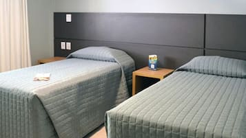 Une chambre d’hôtel avec deux lits simples, une table de chevet en bois sur laquelle se trouvent un livre et une boîte, et une tête de lit grise.