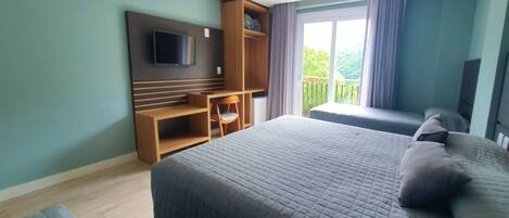 A bedroom with a bed, a TV mounted on the wall, a wooden desk, and a balcony with curtains.